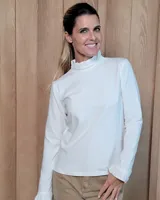 Polera de manga larga en color blanco, confeccionada en algodón. Presenta un cuello alto con detalle de volados y puños con terminación similar.