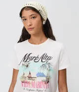 Remera de algodón blanca, de manga corta y cuello redondo, con estampa frontal inspirada en paisajes tropicales y detalles de lentejuelas.