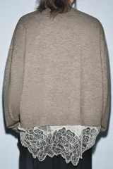 Jersey de punto color beige con cuello redondo y manga larga. Presenta un diseño de bajo combinado con un detalle de encaje en color crema.