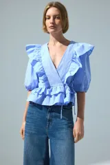 Blusa cruzada celeste a rayas blancas de popelina de algodón, con escote en V pronunciado, mangas cortas abullonadas, volados en el frente y detalle de lazo para atar en la cintura.