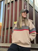 Buzo oversize color beige con bloques de color gris y rojo. Tiene cuello alto y puños acanalados.