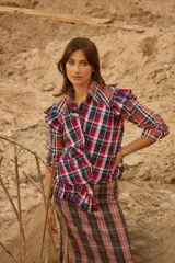 Camisa de diseño original con combinación de telas escocesas en tonos rojo, azul y blanco. Presenta cuello camisero, cierre frontal con botones y volados decorativos en las sisas y en el dobladillo.