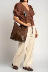 Bolso tipo shopper de tamaño maxi, confeccionado en material efecto gamuza marrón con base en cuero sintético oscuro. Cuenta con una correa ajustable y desmontable trenzada en varios colores.