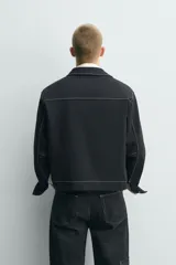 Sobrecamisa de corte regular fit color negro con pespuntes en contraste blancos. Presenta cuello solapa, mangas largas con puños abotonados, bolsillos frontales de vivo y cierre de cremallera oculta por solapa con botones.