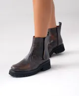 Bota corta tipo chelsea de cuero vacuno color marrón, con suela track de goma negra y elástico lateral.