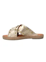 Sandalias tipo ojota con tiras cruzadas en cuero metalizado dorado, decoradas con tachas metálicas y hebilla lateral. Presentan una base con detalle de yute trenzado alrededor del contorno.