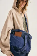 Bolso grande de denim azul, con correa larga ajustable para llevar cruzado o al hombro, bolsillo delantero y parche de cuero sintético con el logo grabado.