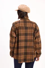 Camisa de corte oversize con estampado de cuadros en tonos marrones y negros. Presenta cuello clásico, cierre frontal de botones metálicos y dos bolsillos con solapa en el pecho.
