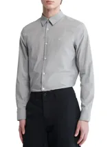Camisa de vestir gris claro de manga larga, con cuello clásico y cierre de botones. Tiene el logo de Calvin Klein bordado en el pecho.