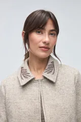 Chaqueta de lana fina sin teñir, con cuello clásico y bolsillos frontales. Presenta detalles bordados en el cuello y en los puños de las mangas. Es una prenda forrada con diseño exclusivo.