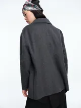 Chaqueta de paño color beige, de corte amplio y estructura clásica. Presenta solapas, cierre frontal con dos botones y bolsillos laterales con solapa.