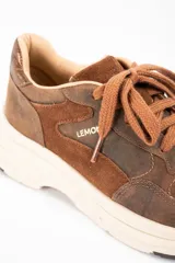 Zapatilla urbana de cuero lavado en tonos marrones, con paneles de gamuza y detalles metalizados en el talón. Presenta cordones al tono y una suela de plataforma de goma en color crema.