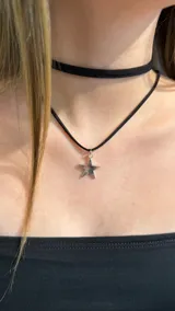 Gargantilla doble de cordón negro con dije metálico en forma de estrella plateada.