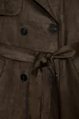 Trench largo de ante sintético color marrón oscuro, de corte cruzado con doble botonadura, solapas amplias y cinturón ajustable del mismo tejido. Cuenta con bolsillos laterales de vivo, mangas largas con trabillas en los puños y detalles en los hombros.