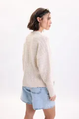 Sweater de punto fantasía color crudo, de corte holgado, con cuello redondo y mangas largas.