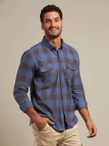 Camisa de franela a cuadros azules y grises, de manga larga con puños abotonados y dos bolsillos frontales con solapa abotonada.