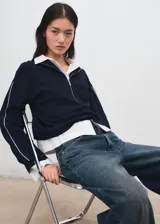 Jersey de punto color negro, con cuello polo y cierre frontal de cremallera, mangas largas y detalles de ribetes claros en las costuras.