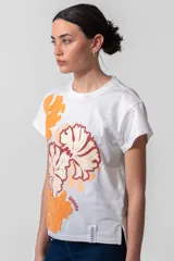 Remera blanca de algodón con cuello redondo y mangas cortas. Estampado frontal con flores en tonos naranja y bordó, y logo de la marca en el ruedo.