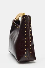 Bolso de mano de efecto acharolado color marrón oscuro, con detalle de tachas metálicas doradas en los bordes. Cuenta con asa rígida metálica dorada y cierre de botón imantado.
