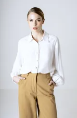 Camisa blanca de manga larga holgada, con cuello camisero, cierre frontal de botones y puños fruncidos con elástico.