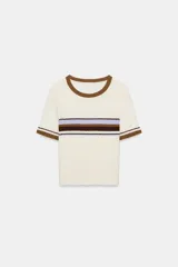 Top de tejido rústico con cuello redondo y manga corta. Presenta un diseño de base color crema con detalles de rayas horizontales en tonos marrón y lila en el pecho y los puños.