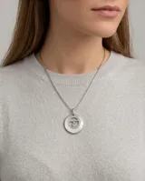Dije circular de plata 925 con incrustación de nácar, borde decorado con circonias y diseño central calado con la palabra mama y una figura de niña.