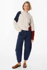 Sweater de punto con diseño de bloques de color en tonos crema y marrón. Presenta cuello redondo, mangas largas y una silueta holgada con detalle de placa metálica decorativa en el lateral.