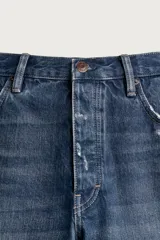 Bermuda baggy fit confeccionada en denim de algodón con lavado azul y efecto rotos en toda la prenda. Presenta diseño de cinco bolsillos, detalles de costuras en las perneras, bajo acabado irregular y cierre frontal con cremallera y botón.