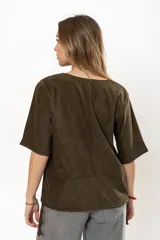 Remera de gamuza color rojo oscuro, con cuello redondo, mangas cortas y detalle de cortes verticales y horizontales que definen la silueta. Presenta cordones ajustables en el ruedo inferior.