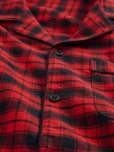 Pijama de hombre compuesto por una camisa de manga larga y un pantalón largo, ambos confeccionados en tela de franela con estampado de cuadros en tonos rojo y negro. La camisa cuenta con cierre frontal de botones y cuello clásico, mientras que el pantalón presenta un corte recto y cómodo.