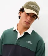 Remera tipo chomba de manga larga, con bloques de color en tonos verde y azul marino, cuello polo blanco y pequeño bordado en el pecho.