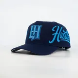 Gorro con visera curva de color azul marino, con diseño ajustable y bordados en color celeste en el frente y los laterales, incluyendo detalles de pedrería en el logotipo frontal.