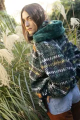 Buzo canguro oversize de paño de lana gris con capucha estampada y cuello de corderito blanco. Cuenta con aberturas laterales en el ruedo y detalles de cuero sintético marrón en el cierre frontal y etiqueta.