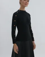 Polera gris de tejido de punto con cuello redondo y mangas largas. Presenta detalle de botones metálicos en los hombros y puños.