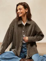 Camisa de pana color crema, con cuello camisero, botones negros en el frente y mangas largas abullonadas con puños.