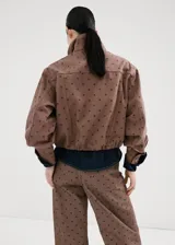 Chaqueta bomber de algodón color marrón con estampado de lunares, cuello embudo, manga larga, bolsillos laterales y cierre oculto con cremallera y botones a presión.
