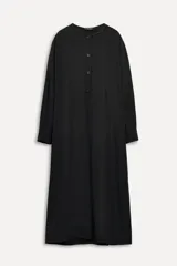 Vestido midi negro confeccionado en viscosa, de corte recto y manga larga con puños abotonados. Presenta cuello redondo con detalle deshilachado, bolsillos laterales ocultos y trabillas en la espalda.