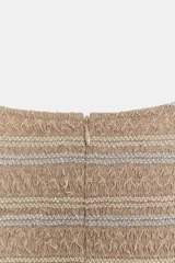 Top color beige con cuerpo de nido de abeja elástico con bordados a contraste, mangas cortas abullonadas y detalle de volante en el bajo. Cuenta con cierre en la espalda con cremallera oculta.