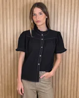 Camisa de manga corta color negro, con cuello alto mao y ribetes con volados. Presenta costuras a la vista en contraste y cierre frontal con botones.