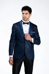 Ambo de ceremonia tipo smoking, compuesto por un saco azul con diseño jacquard y solapa chal de raso al tono, y un pantalón negro satinado de corte slim fit.