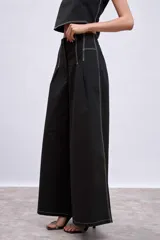 Pantalón marrón de corte palazzo, tiro alto, con pliegues frontales y pespuntes blancos decorativos.