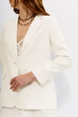 Saco de vestir color blanco hueso, corte recto y holgado, con solapas de muesca, un botón frontal y bolsillos de parche.