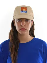 Gorro de gabardina color beige con parche bordado en el frente con un sol y la inscripción YgnA.