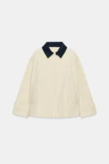 Chaqueta de corte recto confeccionada en algodón con estampado de cuadros. Presenta cuello solapa en color azul marino a contraste, cierre frontal con botones ocultos bajo solapa, bolsillos laterales y mangas largas con trabillas ajustables en los puños.