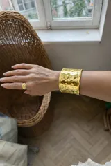 Pulsera rígida tipo brazalete ancho, color dorado, con acabado martillado o texturizado brillante.