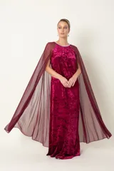 Vestido largo de fiesta color granate, confeccionado en terciopelo con cuello redondo adornado con strass y capa de chifón que nace de los hombros.