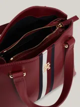 Cartera tote Tommy Hilfiger color borgoña, con doble asa corta y correa larga extraíble. Presenta una franja vertical con los colores de la marca y el logo TH dorado.