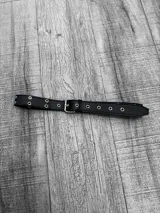 Cinto negro de cuero sintético con hebilla metálica plateada y ojalillos metálicos plateados.