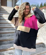 Buzo de estilo canguro con diseño color block que combina paneles en negro, fucsia, beige y un estampado de leopardo. Presenta cuello con cierre de botones a presión y un bolsillo frontal tipo canguro.