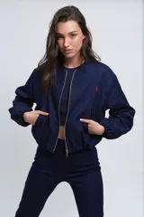 Campera tipo bomber de gabardina de jean color azul oscuro, con cuello a la base, cierre frontal metálico y bolsillos ojal. Presenta mangas largas abullonadas con puños elásticos y costuras con pespuntes en color rojo.